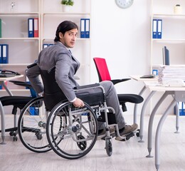 Young handsome employee in wheelchair working in the office