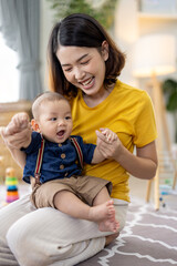 Asian woman playing with her baby boy on the floor with colorful kid toys. Happy baby boy was...