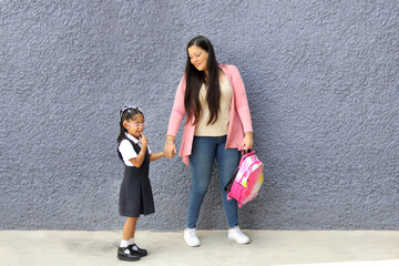 Latina mom walks to class with her 4 year old brunette daughter at back to school with uniform and backpack