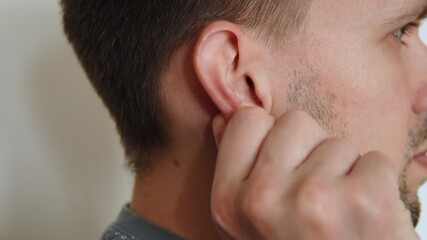 Caucasian man massaging his right ear with his fingers close up. Impact on nerve endings of auricle and earlobe. Nervous movements of anxious person to calm him down.
