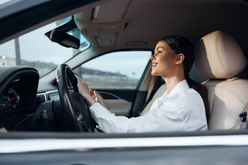 A woman sits in the driver's seat of a car, her hand on the steering wheel, looking directly at the camera with a confident expression, perfectly capturing a moment of attentive driving