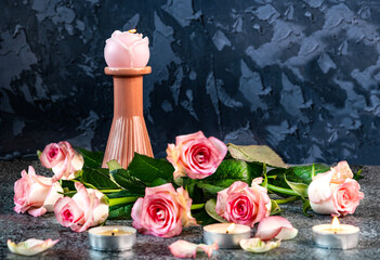Romantic still life with a candlestick and candle in the form of a rose, a bouquet of pink roses on a table on a dark background.