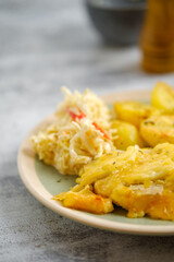 Closeup view of baked pork fillet with melted cheese served with fried potato and cabbage salad