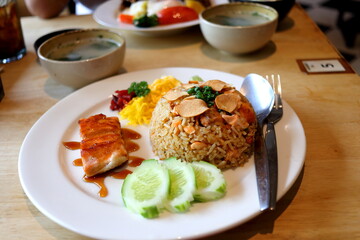 Salmon fried rice and salmon fellet streak on round white dish on wood table with garlic slice fried on top in Thailand.