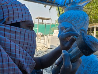 Artisan meticulously sculpting a detailed Red Stone Buddha Statue Using Precision Stone Carving...