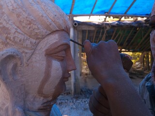Artisan meticulously sculpting a detailed Red Stone Buddha Statue Using Precision Stone Carving...