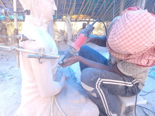 Artisan meticulously sculpting a detailed Red Stone Buddha Statue Using Precision Stone Carving Compass In Odisha, India, tools in hand.