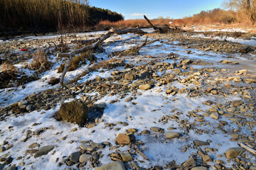 Obraz premium Eye view from below on a frozen river in winter flowing in the middle of the forest