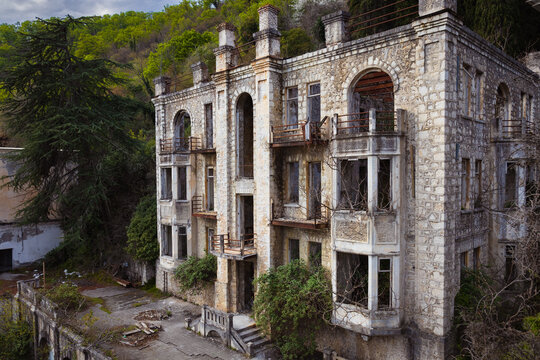 View of an abandoned ruined stone building overgrown with dense tropical tree at the foot of the mountain in old Gagra town in Abkhazia, Georgia