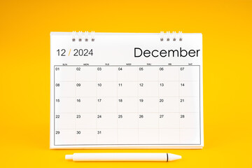 December 2024, Monthly desk calendar for 2024 year and pen on yellow background.