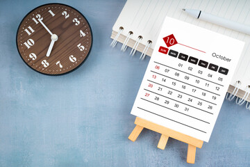 2024 October calendar page and wooden clock on blue wooden.