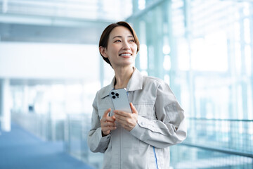 携帯を持つ作業着を着たショートヘアーの女性