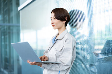 ノートパソコンを持つ作業着を着たショートヘアーの女性