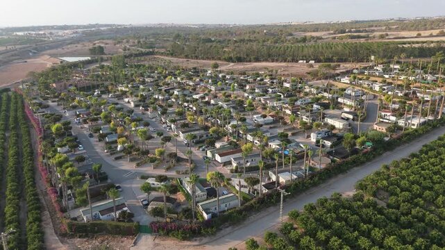 A lateral tracking shot with a drone moves from right to left across a vibrant caravan park near Torrevieja, showcasing the area&rsquo;s lush layout with a lake visible on the left.
