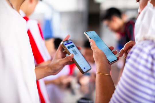 Close-up of people using smartphones to scan QR code for mobile payment or data sharing in a crowded outdoor event, selective focus on hands and devices.