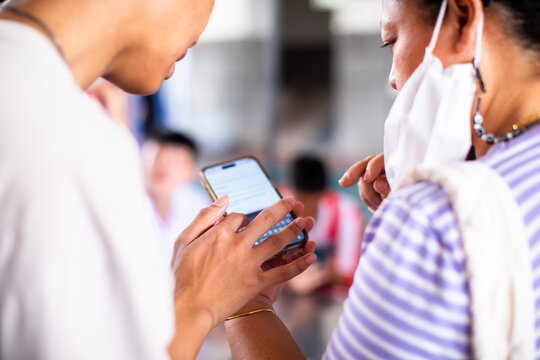 Close-up of people sharing and looking at a smartphone screen together in a crowded public space, focus on hands holding the phone.