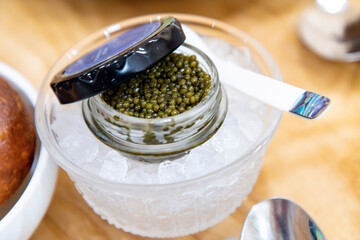 An Open Jar of Ossetra Caviar in a Bowl of Crushed Ice with a Mother of Pearl Spoon