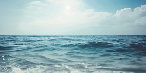Obraz premium Serene ocean scene with blue sea gently disturbed by waves creating rhythmic pattern adding depth. Horizon line separates water from sky with scattered clouds.