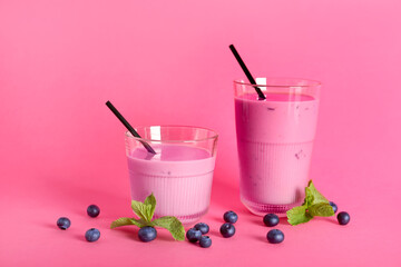 Glasses of fresh blueberry smoothie with mint and berries on pink background