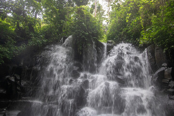 Beautiful hidden waterfall falling over multiple levels. surrounded by black lava stone Kanto Lampo, Bali, Indonesia