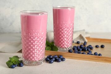 Glasses of fresh blueberry smoothie and wooden tray with berries and mint on white background