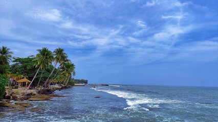 Fototapeta premium Karang Bolong Beach tourist spot, Anyer, Indonesia. Beautiful coastal scenery, blue skies and a wide, choppy sea. Green trees and shacks on the beach, cool for relaxing. 