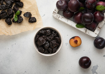 Sweet prunes in glass bowl with ripe plums in wooden box on light kitchen background.Top view.