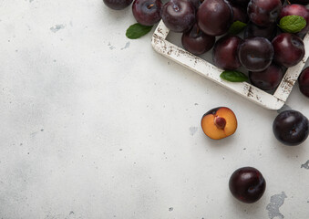 Wooden box of raw ripe purple plums on light kitchen background.Top view.