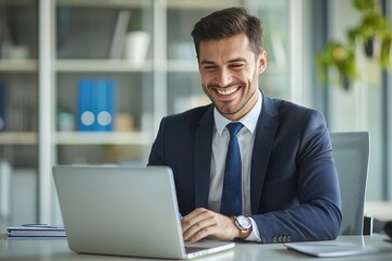 A confident businessman in a suit smiling while working on a laptop in a contemporary office environment, reflecting productivity and professionalism.