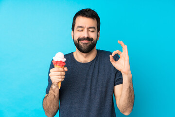 Young man with a cornet ice cream over isolated blue background in zen pose