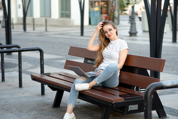 Young girl sitting with laptop on bench with USB charger. Freelance work. Lifestyle. Modern technologies, alternative energy sources.
