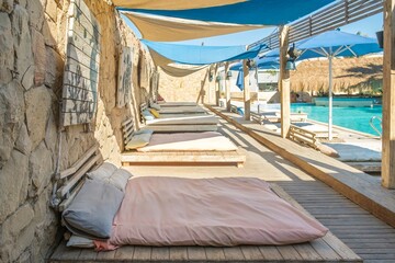 Tranquil beach club scene with empty daybeds, thatched umbrellas, and a sparkling pool under a clear blue sky