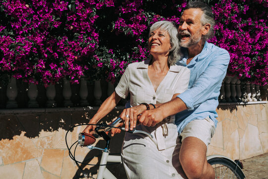 Beautiful happy senior couple dating at the seaside during summertime - Mature married couple in love bonding outdoors and riding bicycle, concepts about elderly lifestyle, transportation and quality 