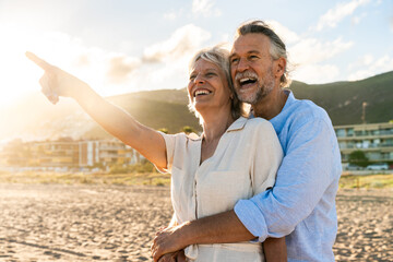 Beautiful happy senior couple dating at the seaside during summertime - Mature married couple in love bonding outdoors at the beach, concepts about elderly lifestyle, relationship and quality of life