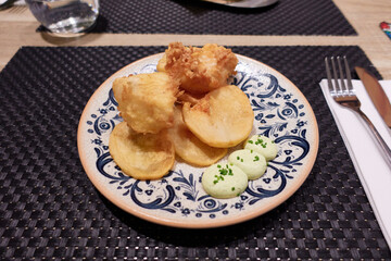 Tempura cod pieces with vegetable chips and dill mayonnaise on a ceramic plate on a placemat in the table in a restaurant