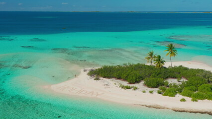 Aerial drone footage of a young woman enjoying her holidays on a desert island, sunbathing near the word holiday written on the beach