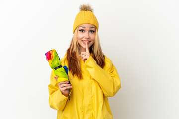 Teenager blonde girl wearing a rainproof coat over isolated white background showing a sign of silence gesture putting finger in mouth