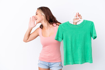 Young Russian girl holding hanger isolated on white background shouting with mouth wide open to the side