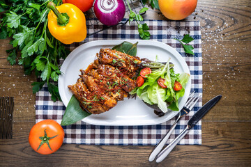 Sticky Pork Ribs with salad, tomato, onion, capsicum, coriander, knife and fork served in dish isolated on napkin top view of italian fastfood on wooden table