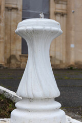 Outdoor drinking fountain in park. A small stream of water gushes out of a white vase