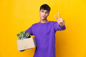 Man making a move while picking up a box full of things smiling and showing victory sign