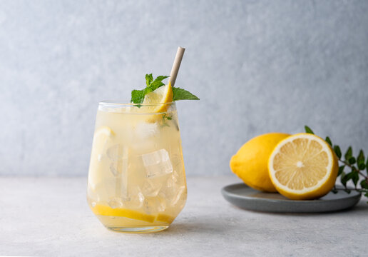 Mojito cocktail with fresh lemon, mint and ice. Refreshing citrus lemonade drink on a light background with fruits.
