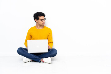 Venezuelan man sitting on the floor with laptop looking to the side
