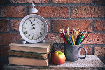 Back to school - clock, books and school supplies on bricks background
