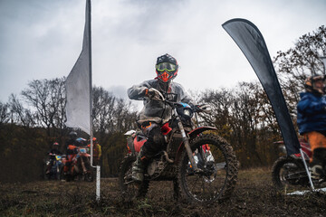 Professional enduro motorcyclist in full moto equipment sitting on crops enduro bike in starting...