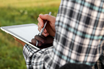 Close-up of an agronomist farmer's hands using a digital tablet and stylus amidst a young...