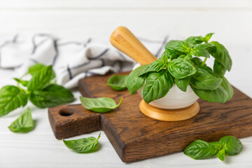 Fresh green basil in a mortar on a textured wooden background. Organic spices and herbs. Vegan. Fresh kitchen herbs. Fresh basil being made into pesto with mortar and pestle.Copy space. Place for text