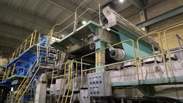 Roller of transmission rotates moving conveyor belt on production line. Large metal shaft turns on papermaking equipment at factory