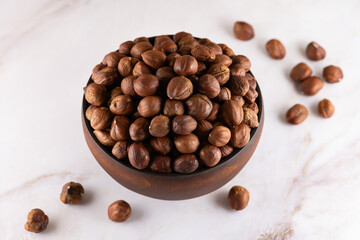 Hazelnuts in a wooden bowl on marble countertop. Whole, dried and shelled nuts of filbert, ready to eat as snack, close-up, high resolution.