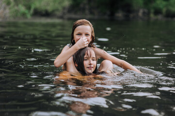 Fototapeta premium Two beautiful girls, happy children, girlfriends play, have fun, laugh, jump in the water at sea. Photography, portrait, childhood concept.